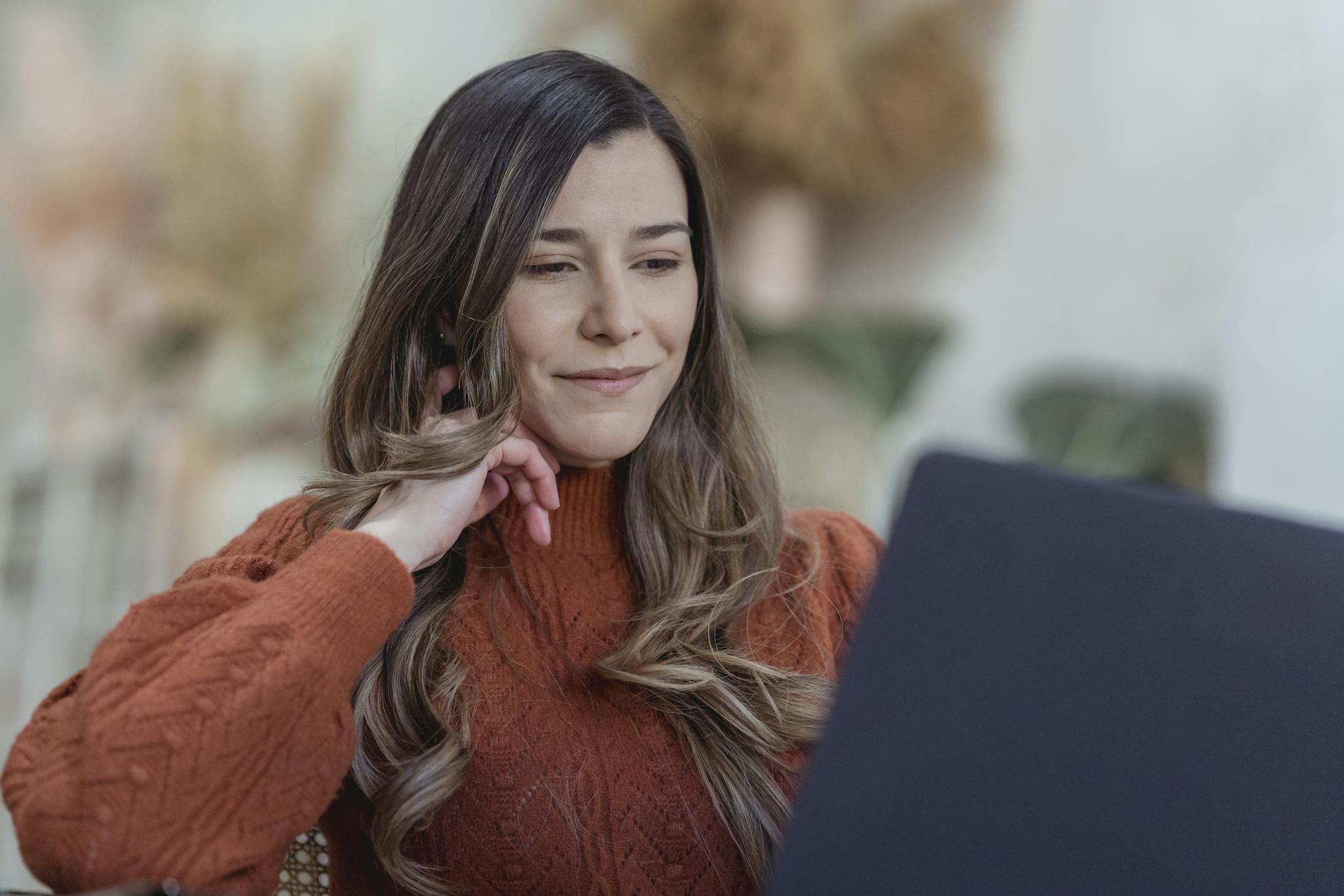 Woman in a sweater working on a laptop, exuding confidence and focus in a cozy, indoors setting.